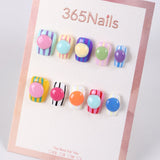 Uñas postizas con diseño de rayas y botones de caramelo de 365Nails.