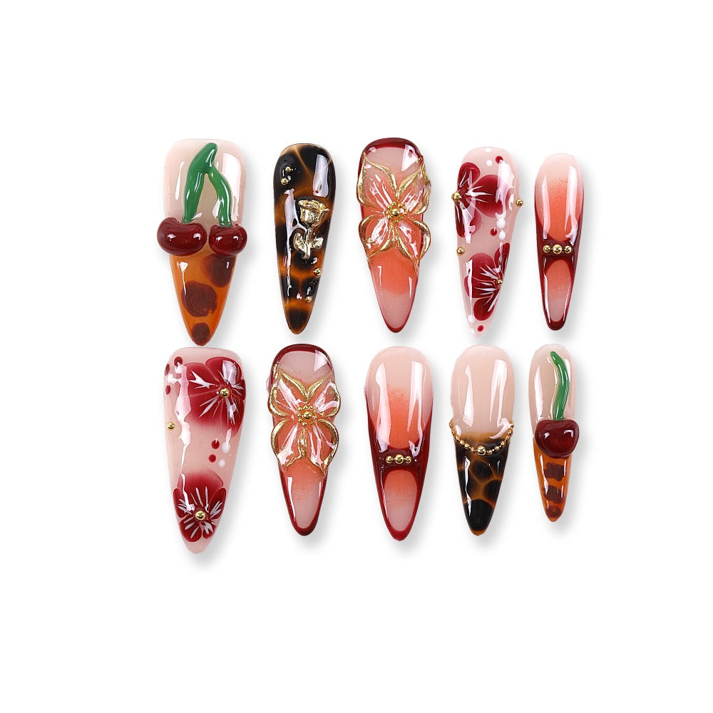 Uñas postizas 365nails con base nude, degradado rojo con efecto carey, cerezas y diseño floral, estilo stiletto/almendrado.