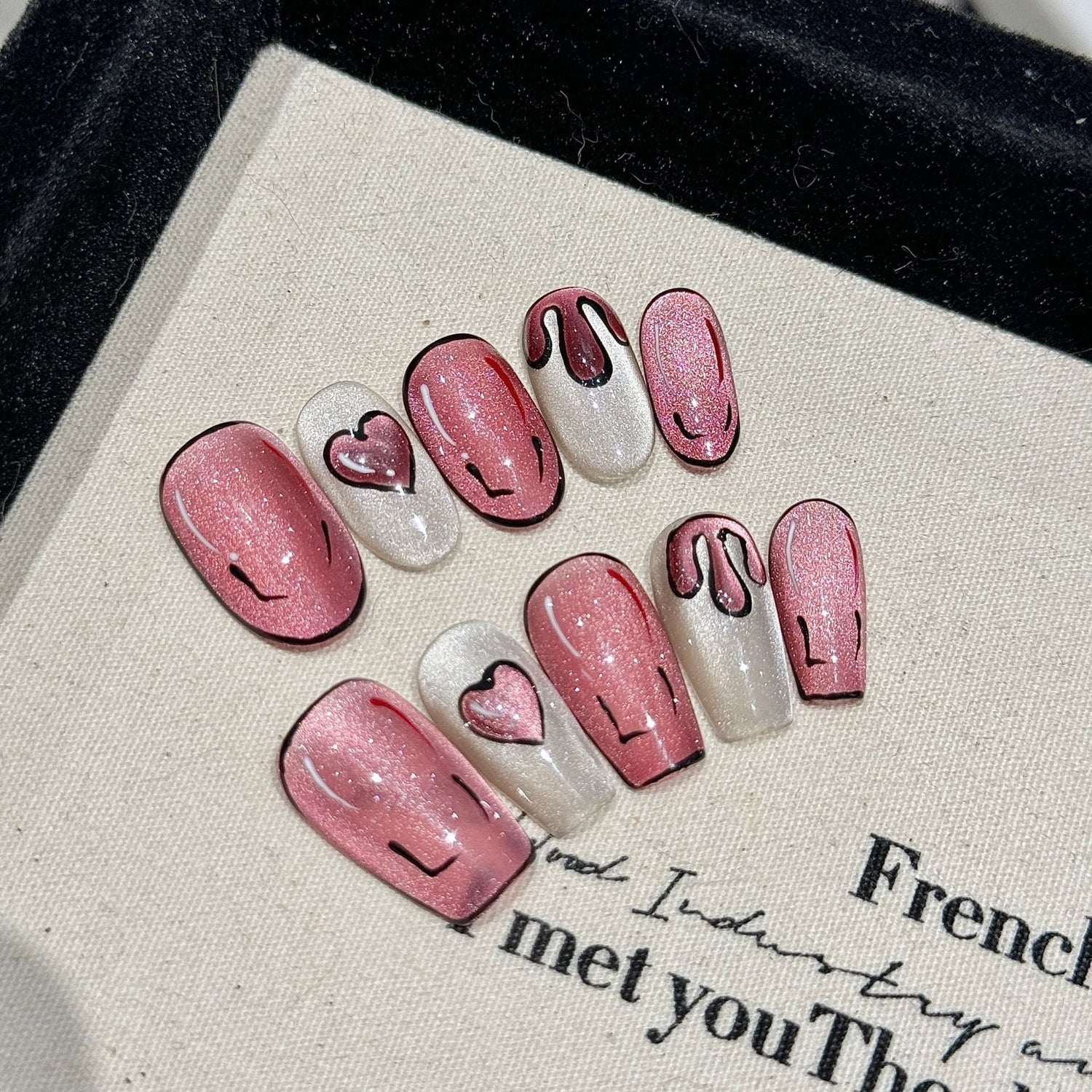 Hand-painted cartoon and glitter cat eye handmade almond press-on nails in pink with heart designs, shown as finished salon-ready press-on nails