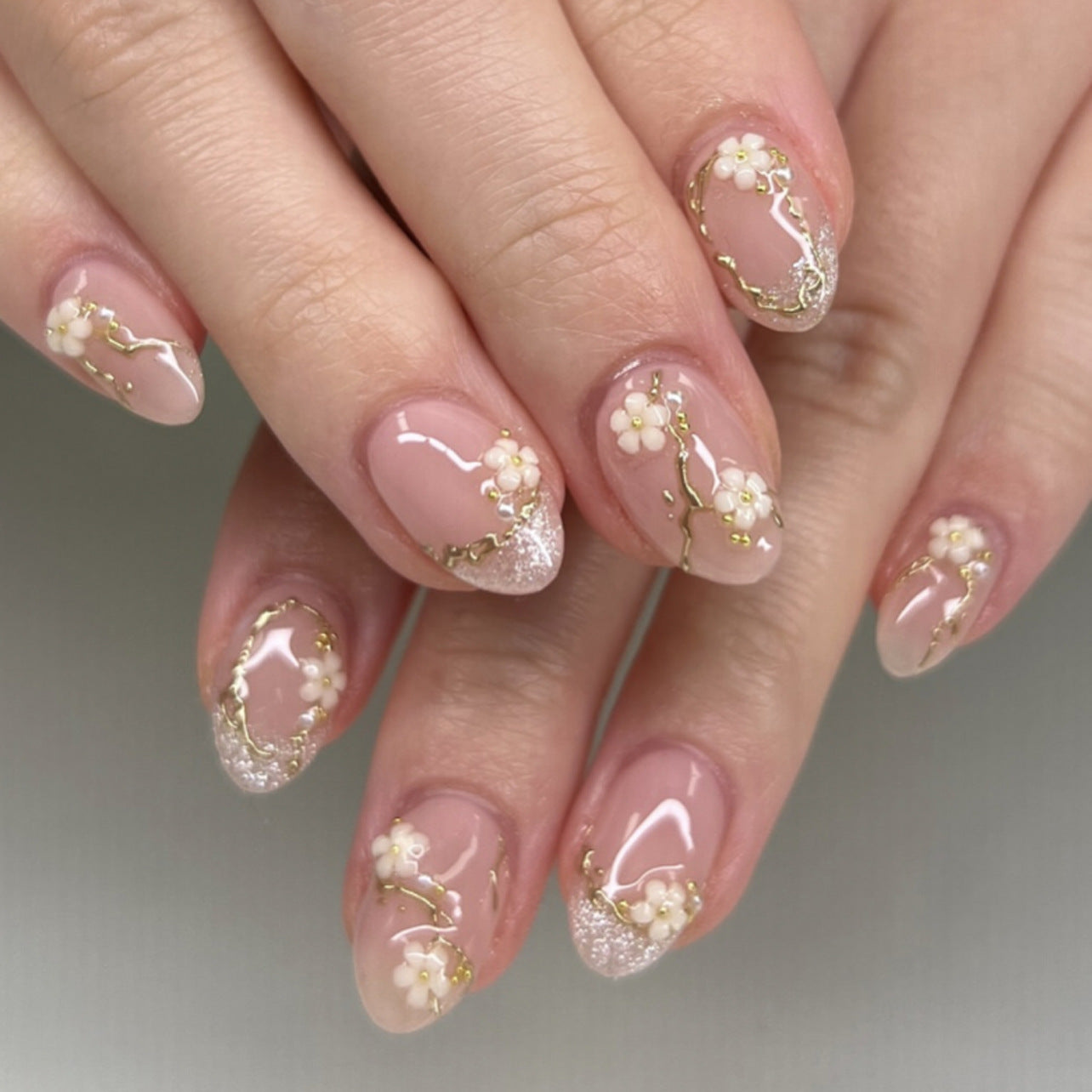Soft pink floral almond press-on nails with gold details displayed on a hand