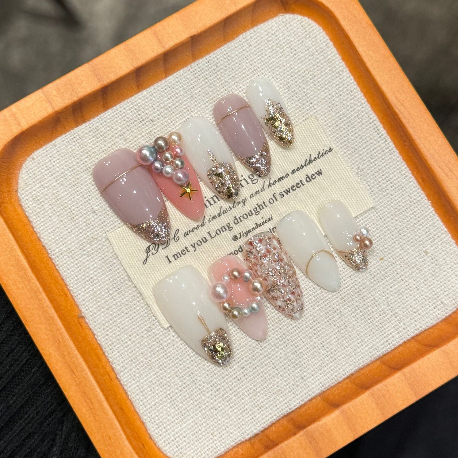 Pink and white glitter press-on nails with pearl and gold accents arranged on a display stand, representing a private-label brand packaging and launch concept.