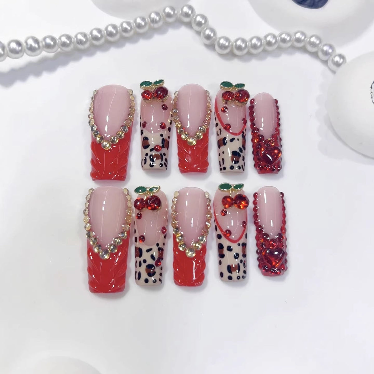 Long square red cherry press-on nails with glossy red finish, rhinestone cherry accents, and nude base, arranged for wholesale salon retail inventory planning.
