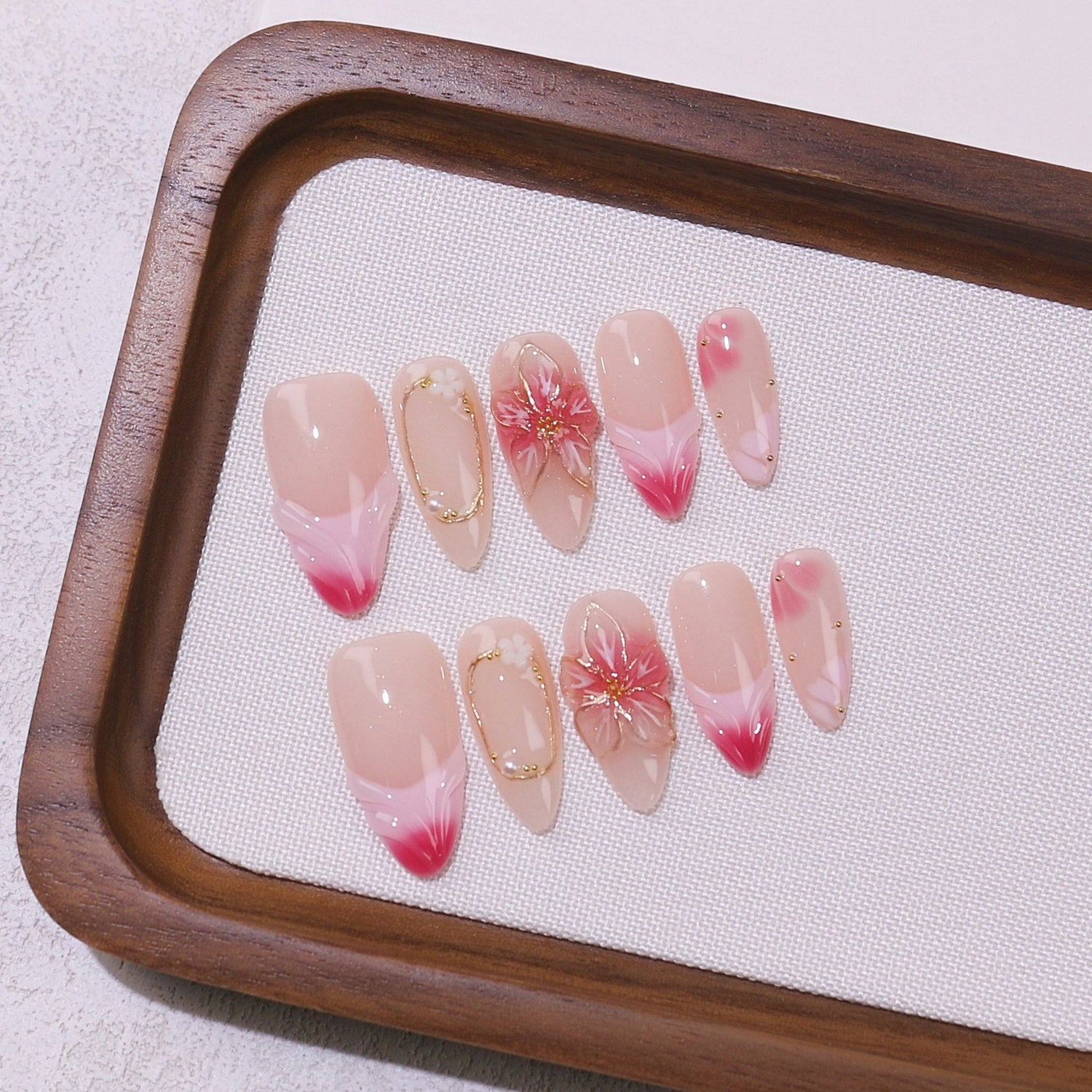 Blush pink and nude gradient almond press-on nails with delicate cherry blossom floral 3D accents and gold details