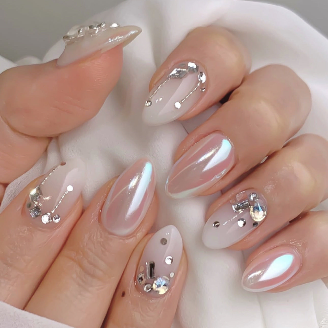 Iridescent pearl chrome crystal almond press-on nails arranged as a wholesale set, showing glossy silver, pearl, and crystal finishes in multiple sizes.