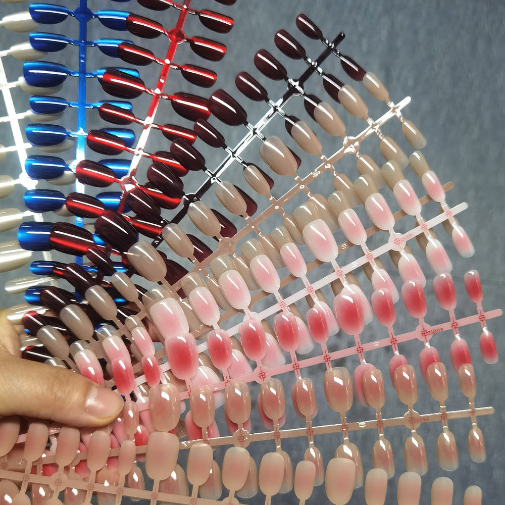 Short oval solid color press-on nails in nude and red shades displayed on a hand model, showcasing everyday wear styles.
