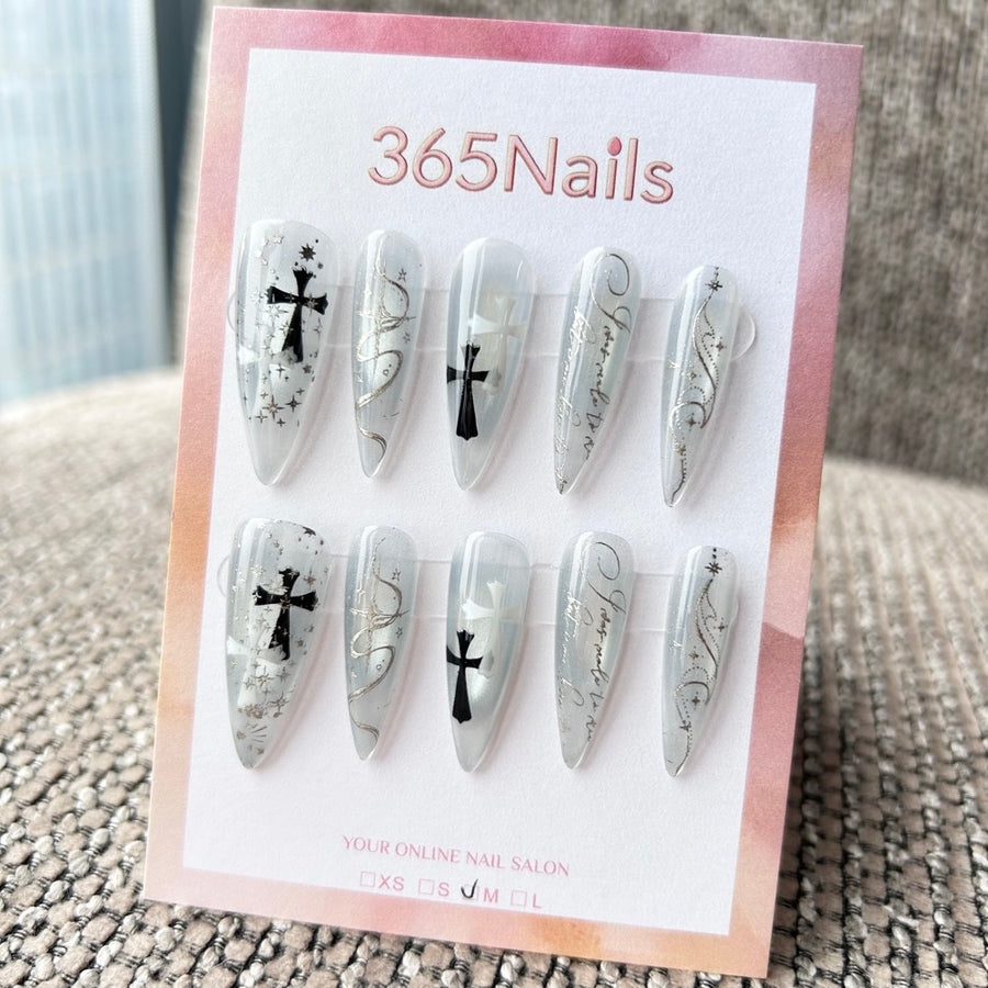 Femme Fatale : « Écriture glacée » – base translucide bleu‑gris avec lettrage argenté, croix gothiques et étoiles — ongles press-on longs forme stiletto