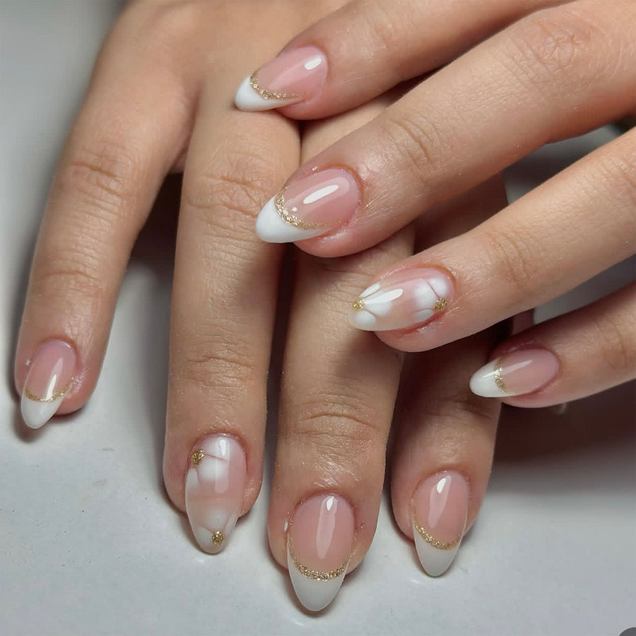Hand wearing almond press-on nails with nude pink base, white French tips and gold glitter line