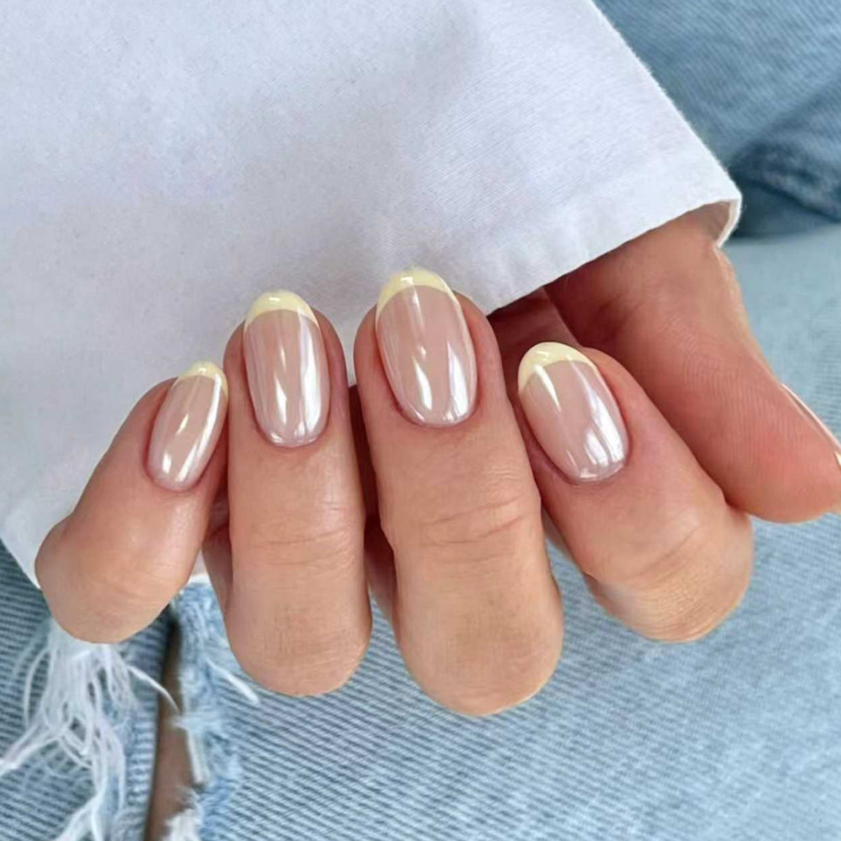 Hand wearing short round nude press-on nails with yellow French tips