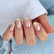 Hand wearing short round nude press-on nails with yellow French tips