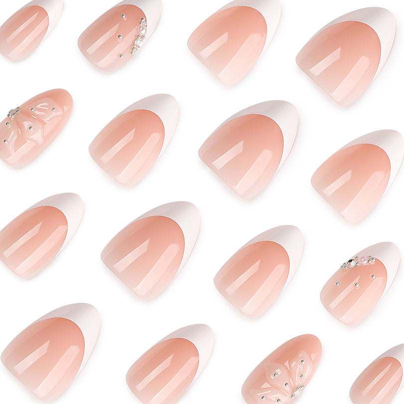Close-up of many nude French almond press-on nails with white tips, floral accents and rhinestones.
