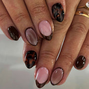 Hand wearing glossy dark-brown French tip almond press-on nails with sheer pink base and tortoiseshell accent nail