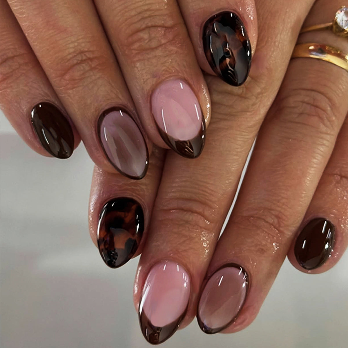 Hand wearing glossy dark-brown French tip almond press-on nails with sheer pink base and tortoiseshell accent nail