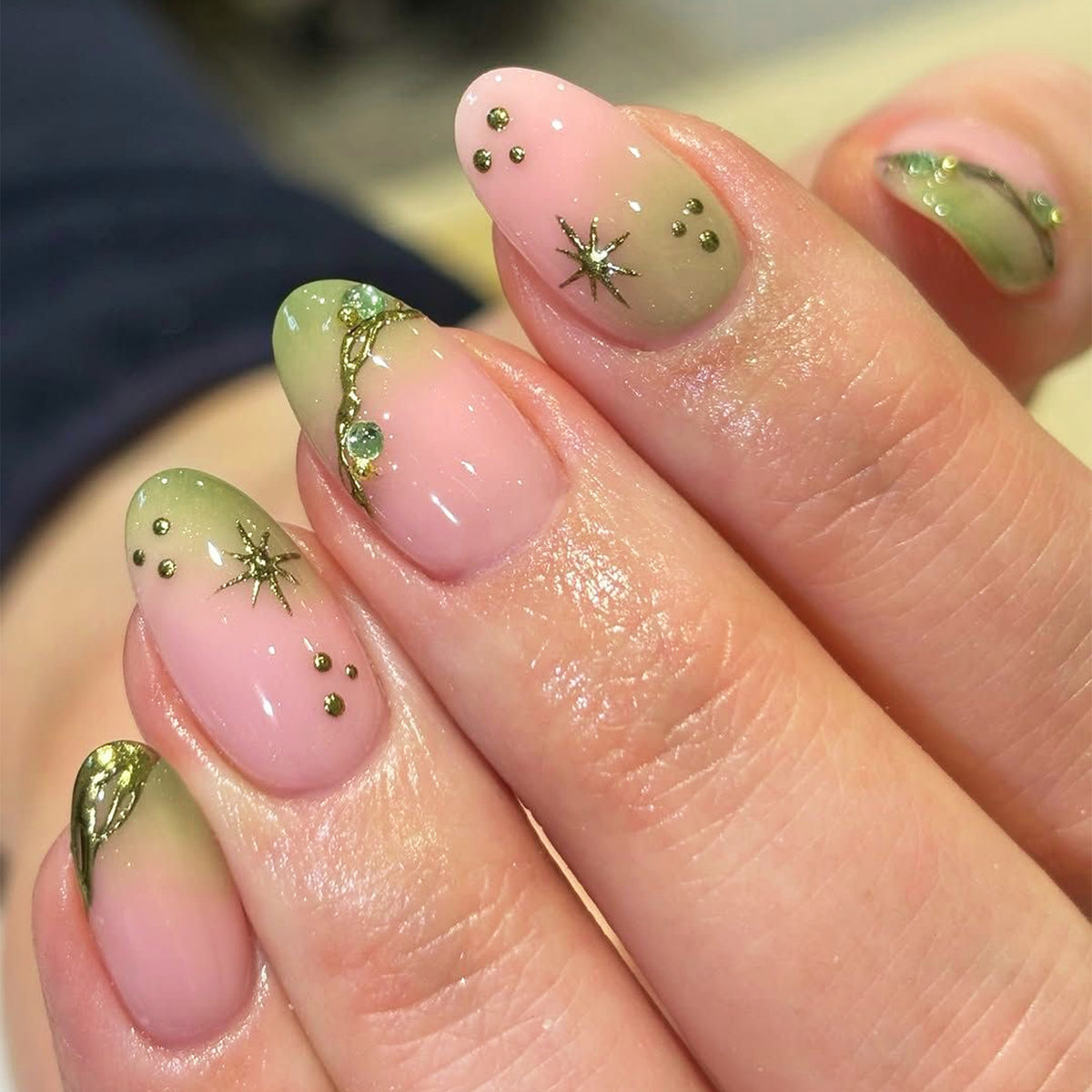 Hand wearing green and pink French almond press-on nails with gold charms