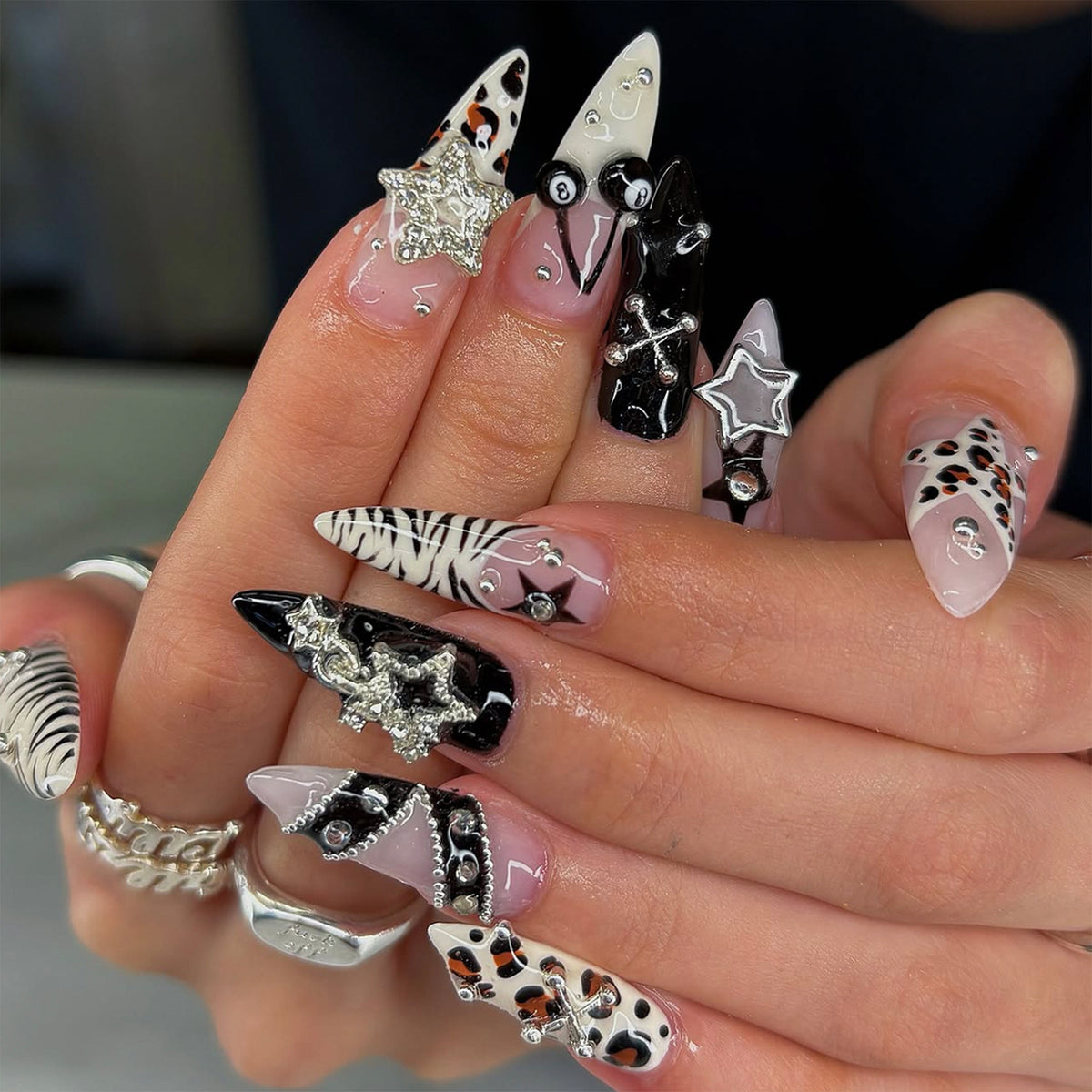 Hand wearing long gothic press-on nails with black, pink, zebra, leopard, star and 3D charm designs.
