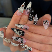 Hand wearing long gothic press-on nails with black, pink, zebra, leopard, star and 3D charm designs.