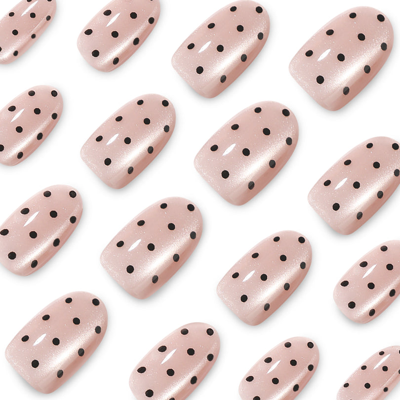 Close-up of glossy nude pink nails with black dots and shimmer
