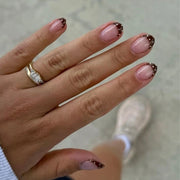 Hand wearing almond press-on nails with light pink base, dark brown French tips and white polka dots