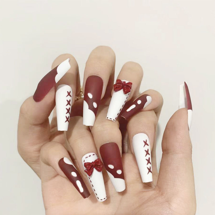 Hand wearing long coffin press-on nails in matte red and white French designs with red bow charms