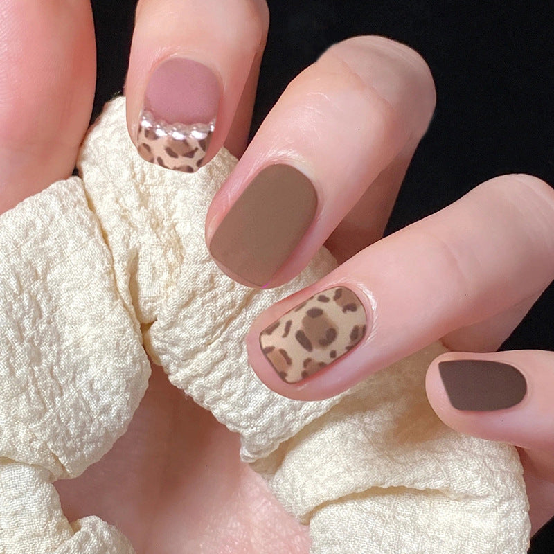 Hand wearing short matte brown press-on nails with leopard print and pearl french tips