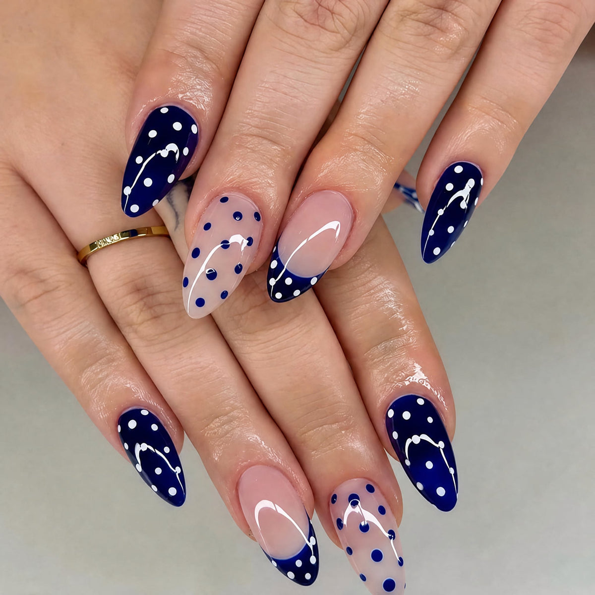 Hand wearing deep blue and nude almond press-on nails with polka dots