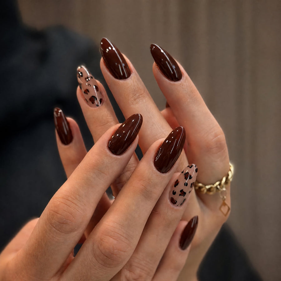 Hands with long almond dark brown glossy press-on nails and leopard print accent nails