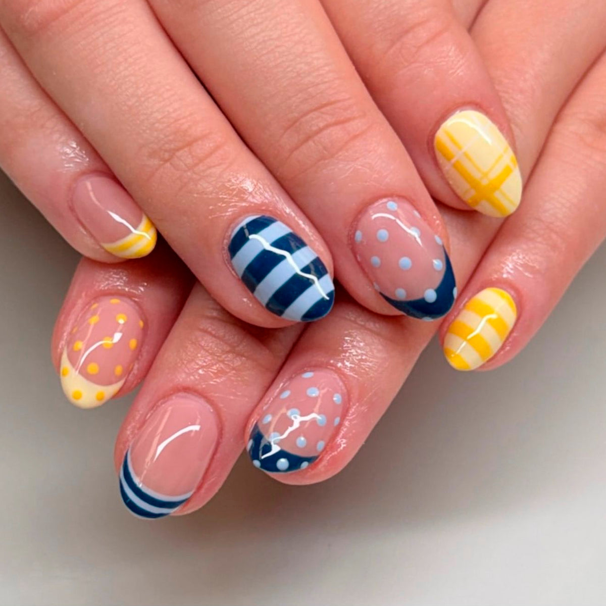 Hand wearing press-on nails with navy polka dots, stripes and yellow cross design