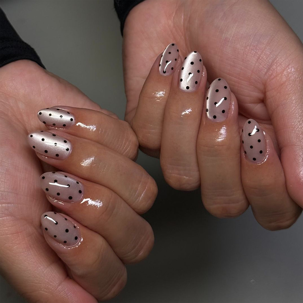 Hands wearing short nude pink press-on nails with black polka dots and cat-eye shine