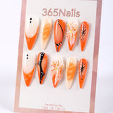 Uñas postizas 365Nails color naranja soda con degradado, borde francés negro y detalles de pétalos con forma de estrella.