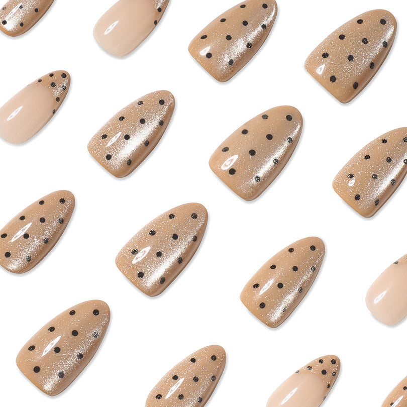 Close-up of nude almond nails with black polka dots scattered on white surface