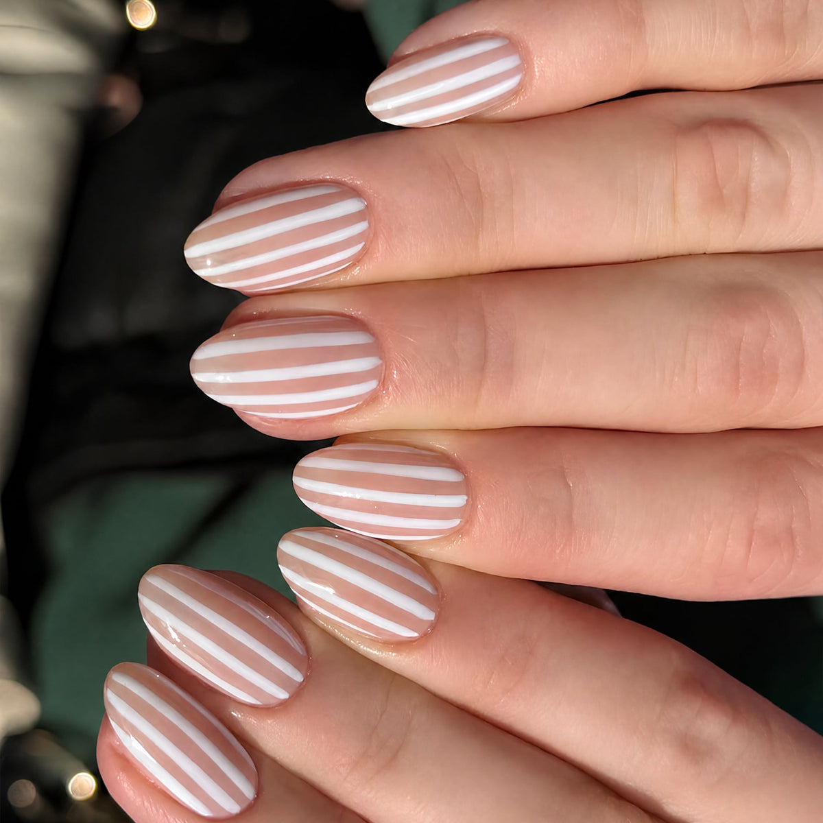 Hand wearing short almond nude and white striped press-on nails