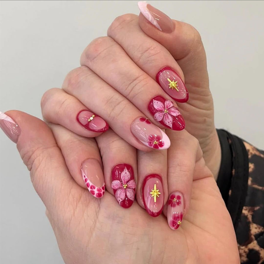 Hand wearing almond-shaped press-on nails in pink and berry tones with 3D flowers