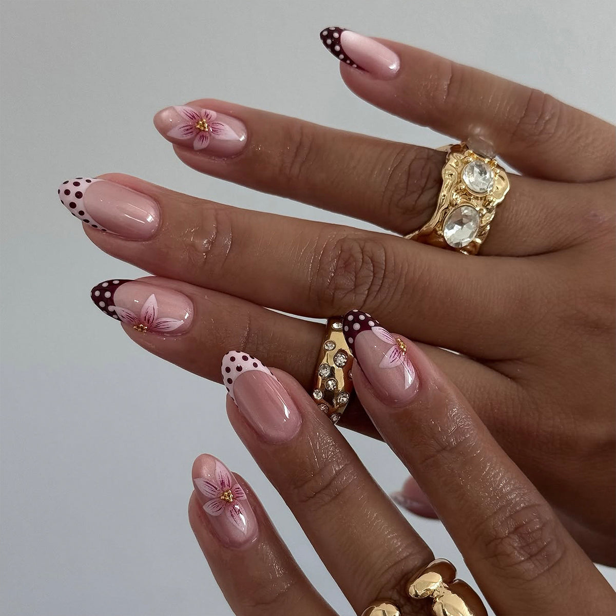 Hand wearing nude almond press-on nails with polka-dot French tips and pink flower art