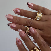 Hand wearing nude almond press-on nails with polka-dot French tips and pink flower art