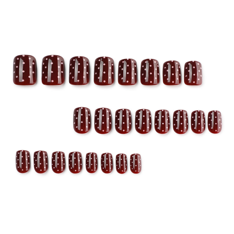 Twenty-four dark red press-on nails with white dots arranged in rows.