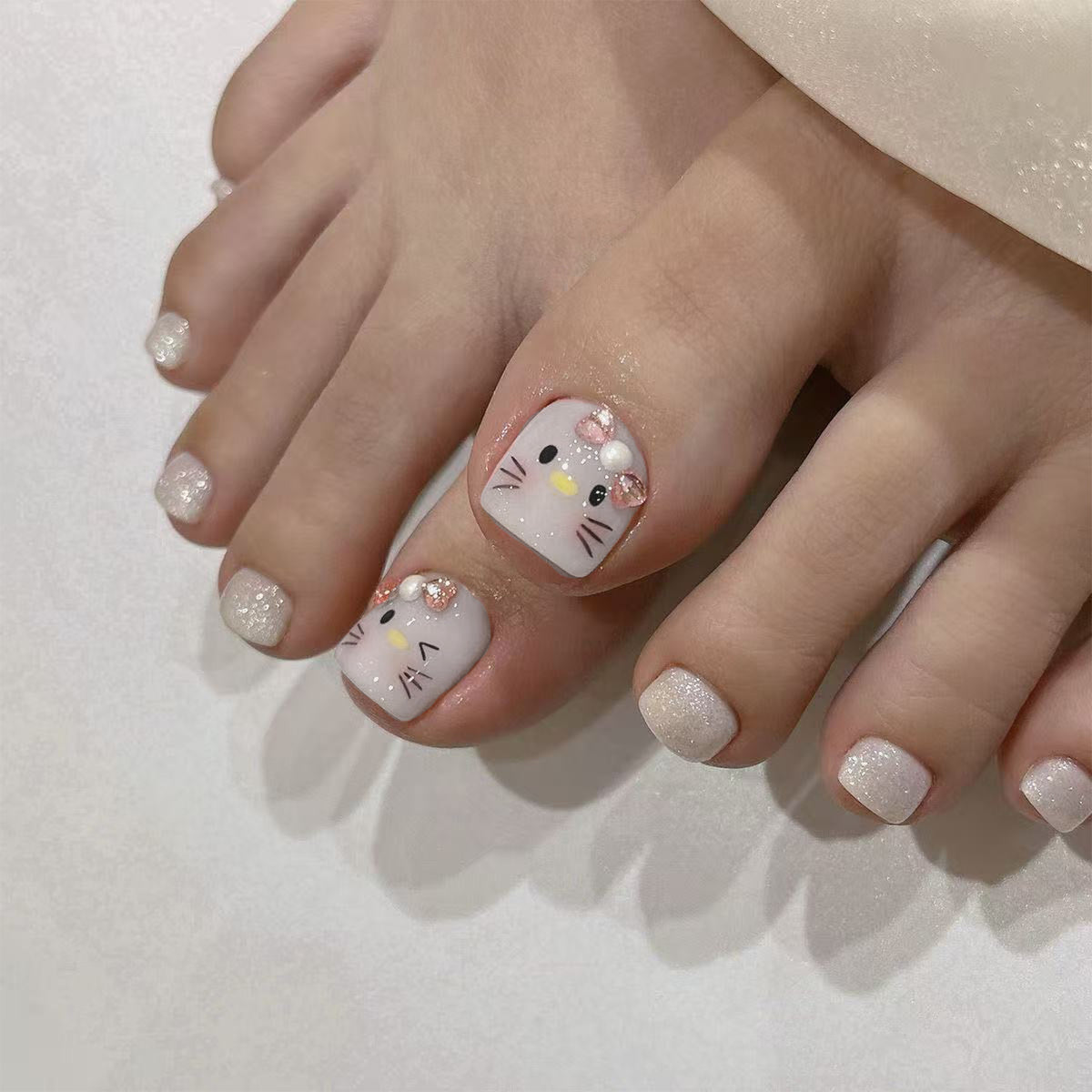 Foot wearing glossy white press-on toenails with cute cat faces and pink bow charms.