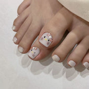 Foot wearing glossy white press-on toenails with cute cat faces and pink bow charms.