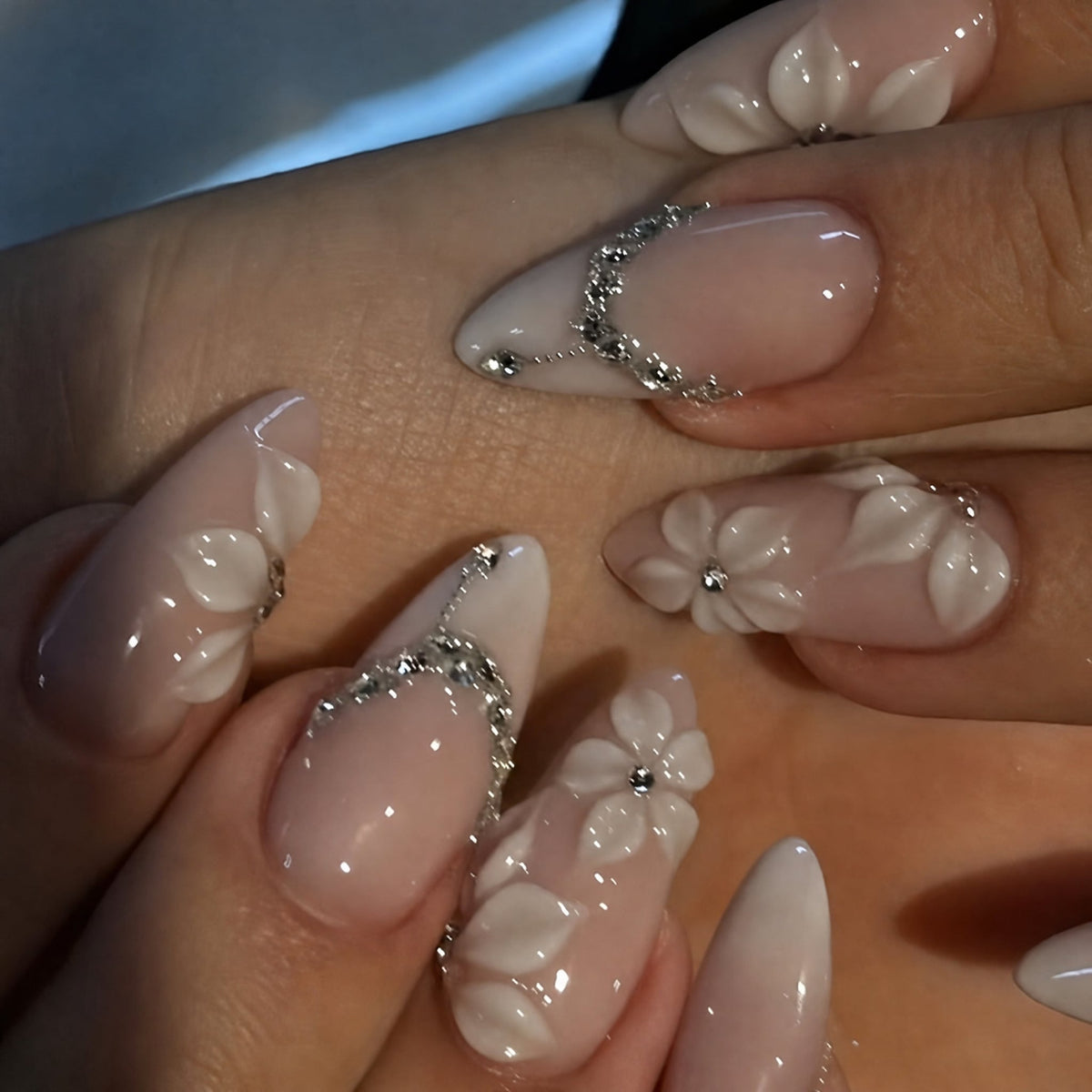 Close-up of a hand wearing pink almond press-on nails with 3D white flower and rhinestone accents