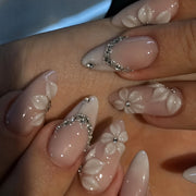 Close-up of a hand wearing pink almond press-on nails with 3D white flower and rhinestone accents