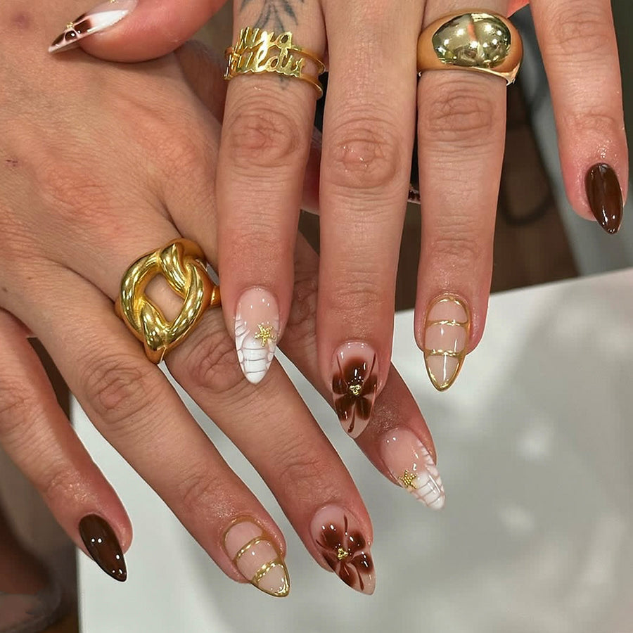 Hand wearing almond press-on nails with brown floral and gold accents