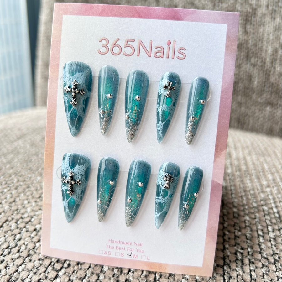 Femme Fatale : « Dentelle abyssale » – aura vert sarcelle profond avec motif dentelle blanche, pointes pailletées argentées et breloques croix — ongles press-on longs forme stiletto