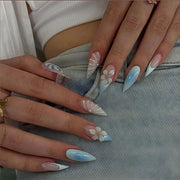 Hands wearing short almond press-on nails with blue French tips and 3D flower charms