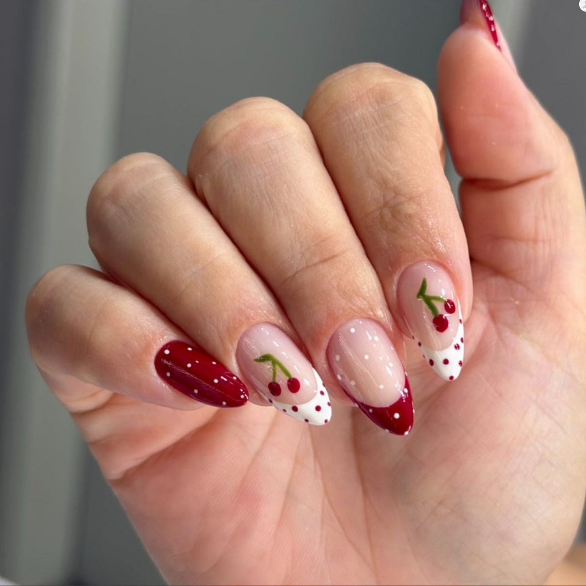 Hand wearing almond press-on nails with cherry art, red French tips and polka dots