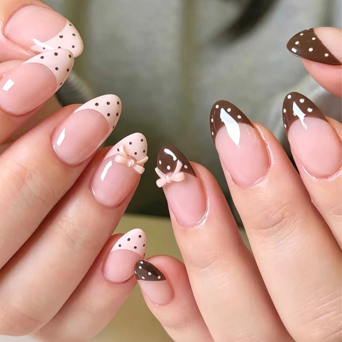 Hand wearing almond press-on nails with pink base, white and dark brown French tips with polka dots and bow charms