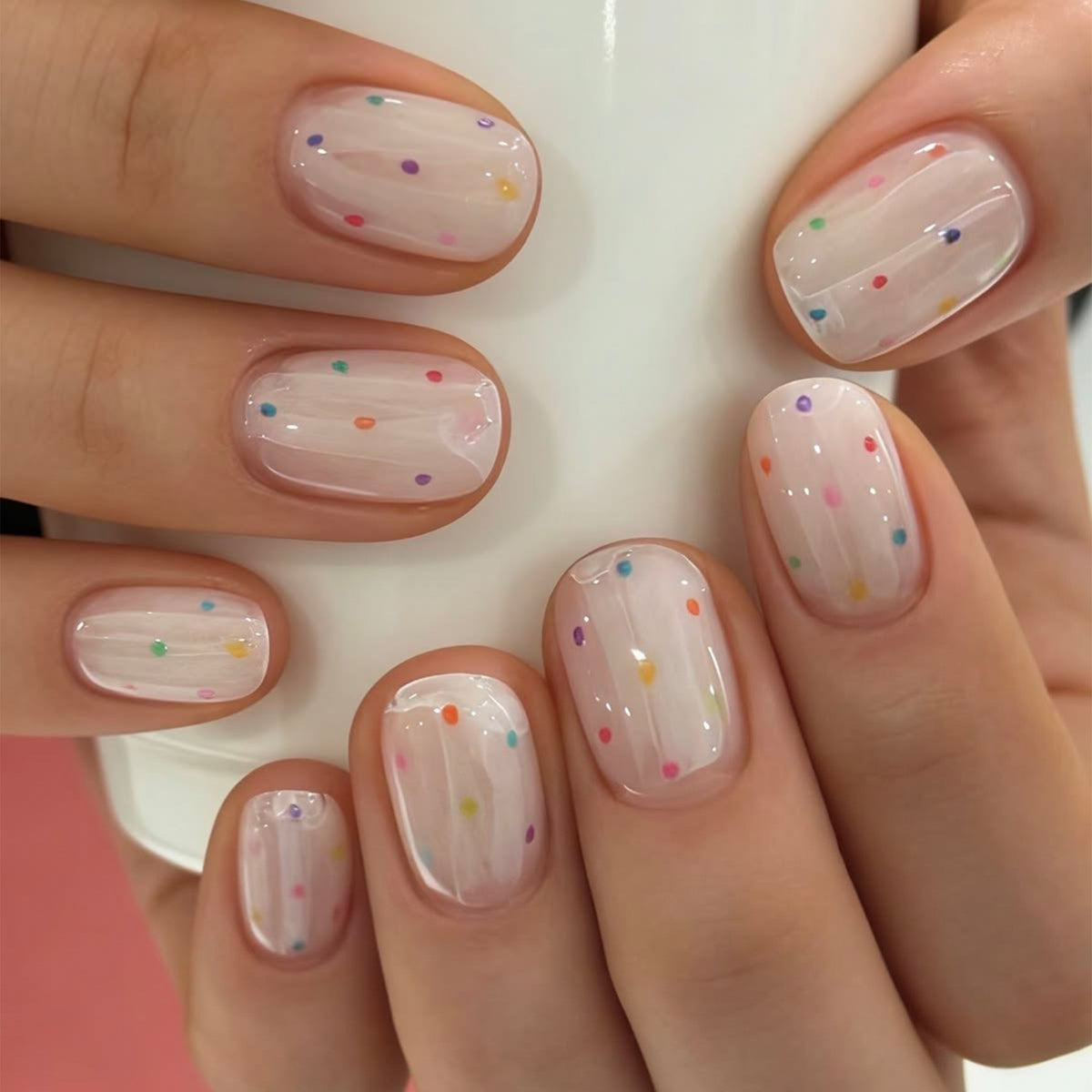 Hand wearing short round press-on nails with colorful polka dots and a sheer white base.