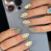 Hand wearing sheer green press-on nails with black polka dots
