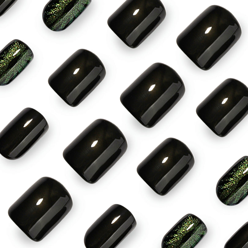 Close-up of glossy black and green cat-eye press-on nail tips