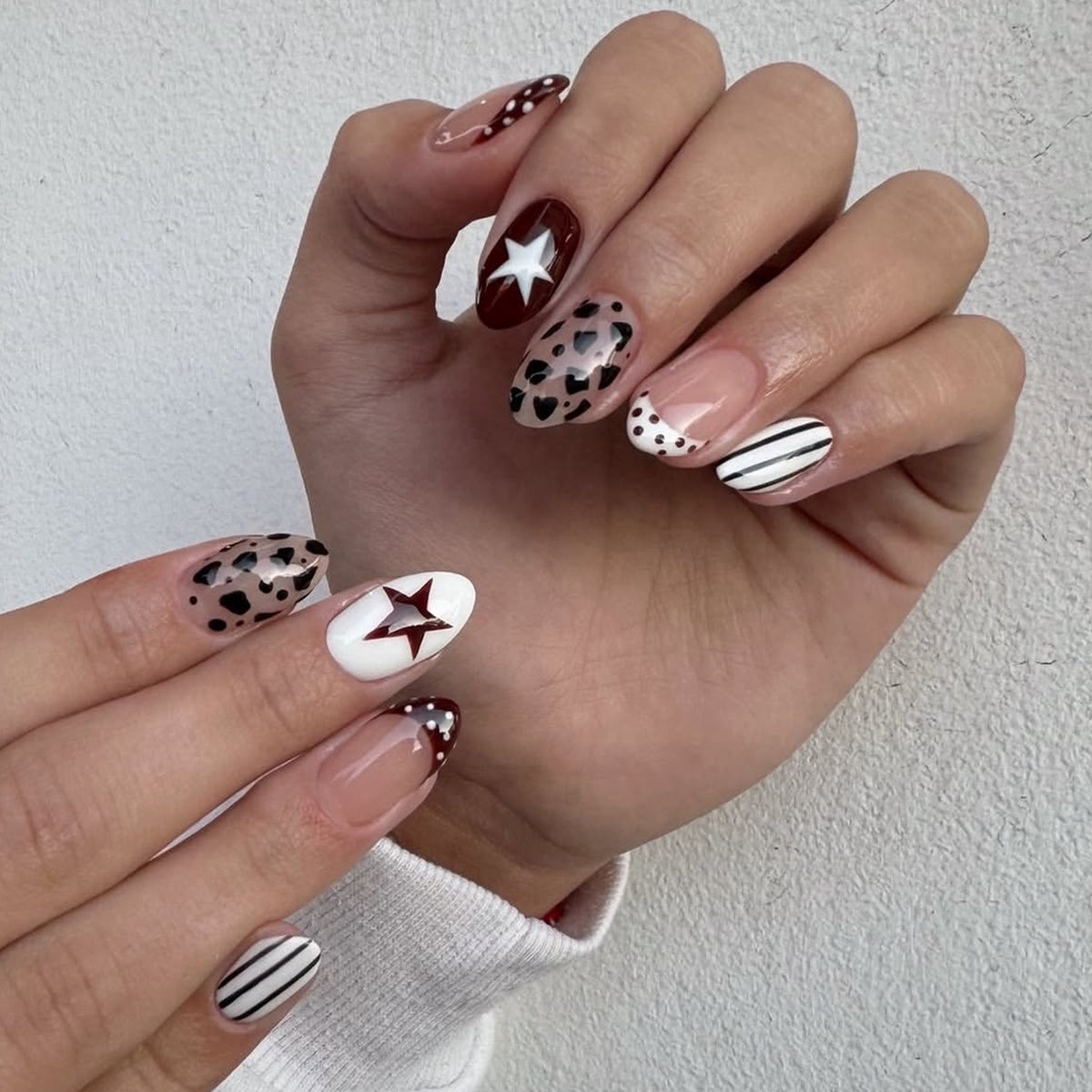 Hand wearing short almond press-on nails with leopard print, stars, stripes and dotted French tips.