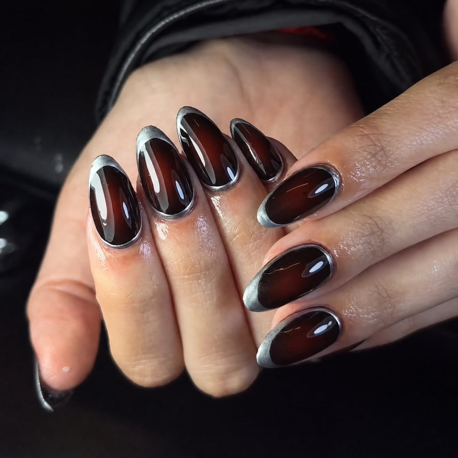 Hand wearing glossy dark burgundy almond press-on nails with silver metallic outline