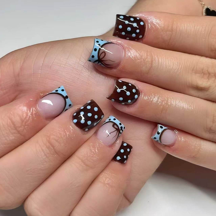 Hand wearing short square press-on nails with black polka dots and light blue french tips