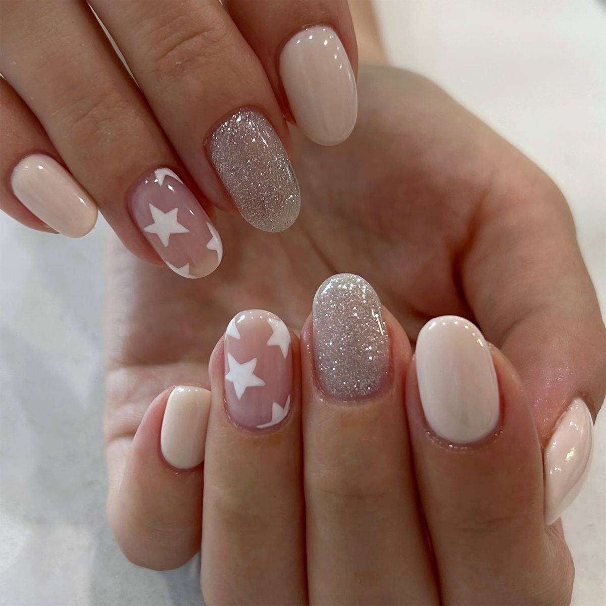 Hand wearing nude and pink press-on nails with white star designs and glitter accent nails